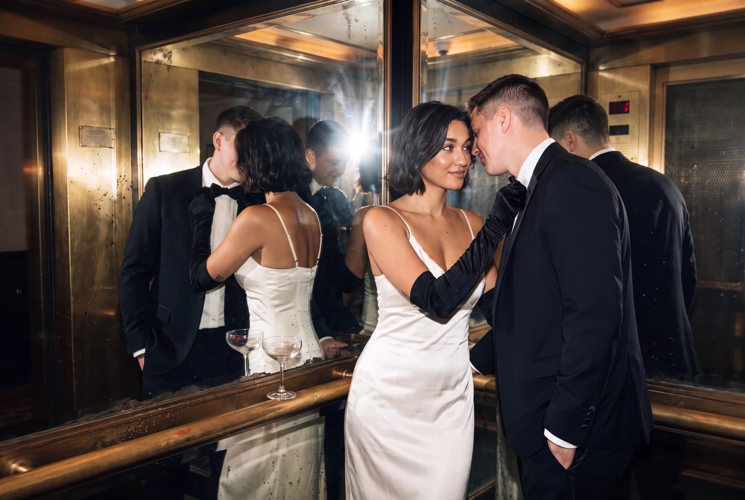 A couple sharing an intimate moment in a mirrored brass elevator, dressed in ivory and black