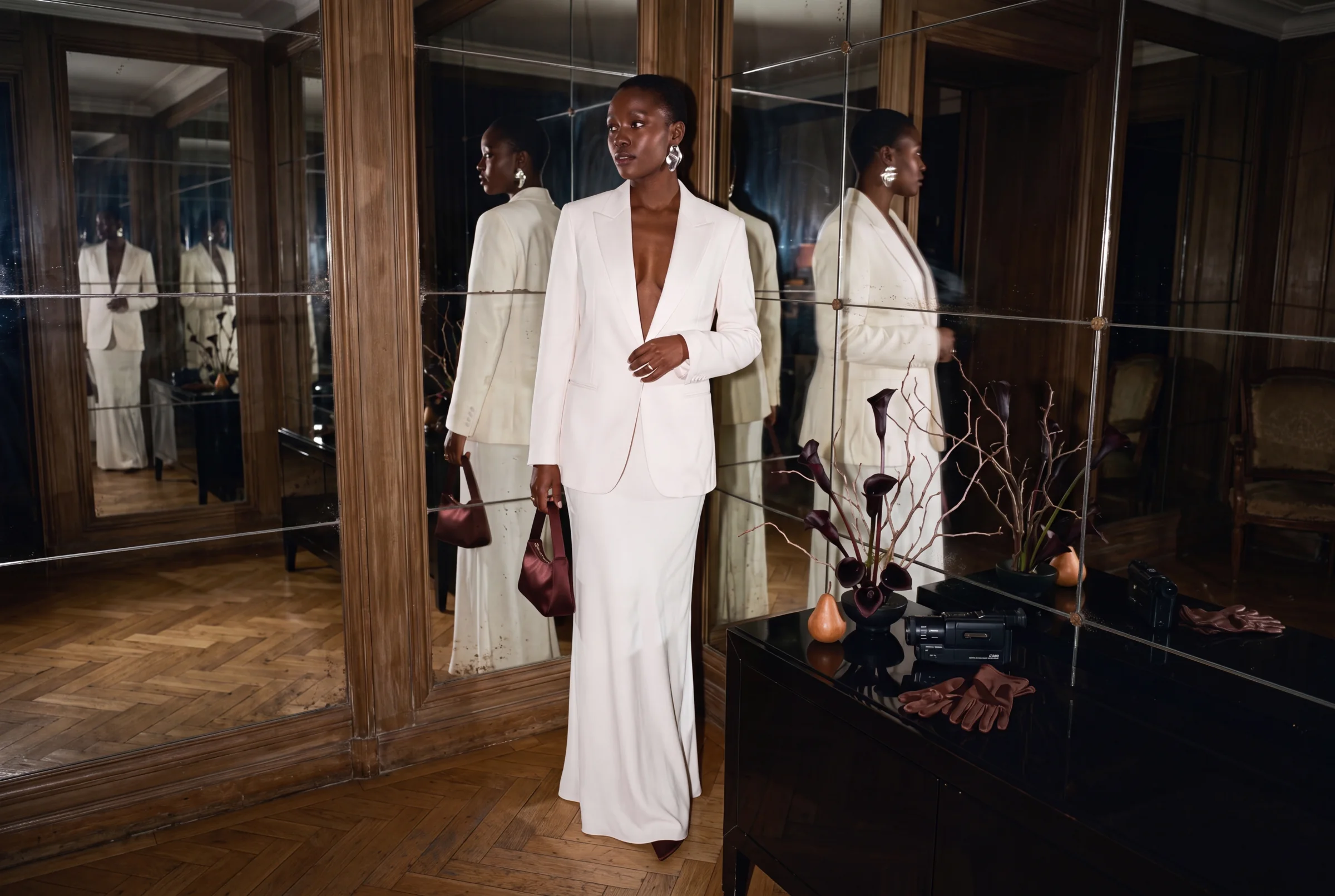 A fashion-forward bride in soft ivory tailoring surrounded by oxblood accessories and sculptural autumn florals