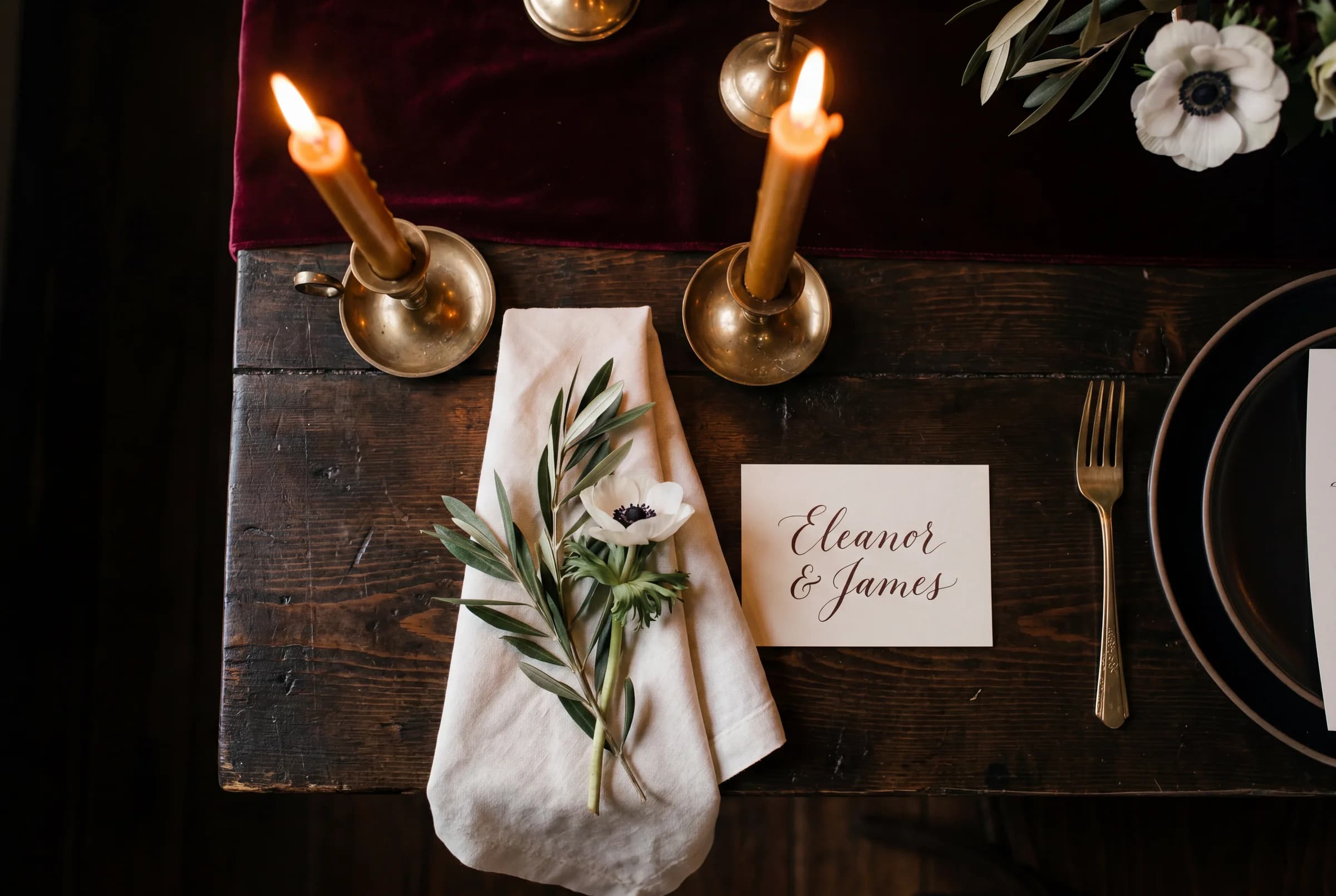 A candlelit wedding tablescape with cream linens, brass candleholders, and white anemones shot from above